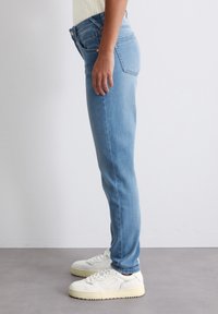 Heledad sinises teksades, millel on slim fit lõige, klassikaline viie tasku disain ja keskmise kõrgusega vöökoht. Kandmisega valged tossud.