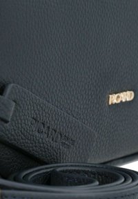 Borsa in pelle blu scuro con superficie testurizzata. Presenta un logo dorato e una tracolla arrotolata. Comprende un'etichetta impressa con "Picard Dal 1928."