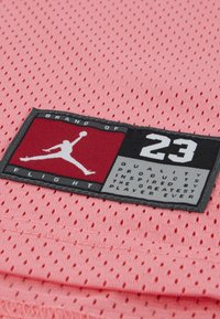 Ροζ ύφασμα από δίχτυ με ορθογώνια μαύρη και κόκκινη ετικέτα που διαθέτει λευκό περίγραμμα λογότυπου, κείμενο και στοιχεία επωνυμίας.