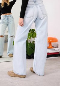 Vaaleansiniset leveälahkeiset farkut, joissa on korkeavyötärö ja kulutuksia. Niissä on viiden taskun malli ja kontrastitikkaukset. Yhdistetty beigenvärisiin kenkiin.