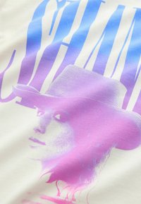Portrait d'une femme portant un chapeau à large bord dans des tons rose et violet avec de grandes lettres bleues stylisées en arrière-plan.