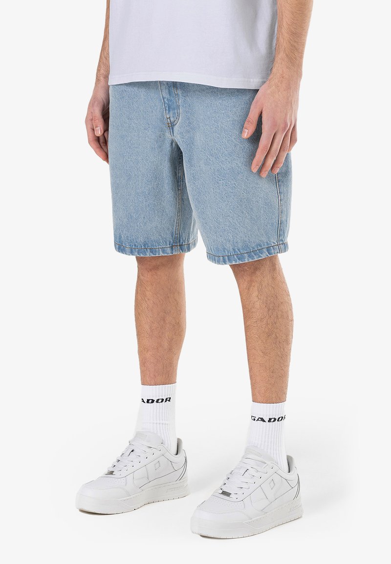 Lyseblå denimshorts med avslappet passform, rå kant og to sidelommer, kombinert med hvite joggesko og stripete sokker.