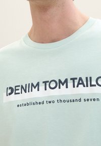 Mintově zelené bavlněné tričko s bílým a tmavě námořnickým grafickým potiskem s nápisy "DENIM TOM TAILOR" a "založeno dva tisíce sedm".