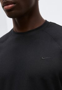 Κοντινό πλάνο ενός ατόμου που φοράει μαύρο φούτερ Nike με εμφανές μαύρο κεντημένο λογότυπο στο στήθος.