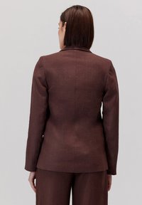 Brązowa lniana marynarka o dopasowanym kroju, z klapami, długimi rękawami i gładkim wykończeniem. Posiada czysty tył z subtelnymi szwami oraz gładką fakturę.