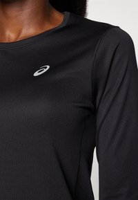 Camiseta deportiva negra de manga larga con cuello redondo, hecha de una tela suave y ligera. Presenta un pequeño logo reflectante en el pecho.