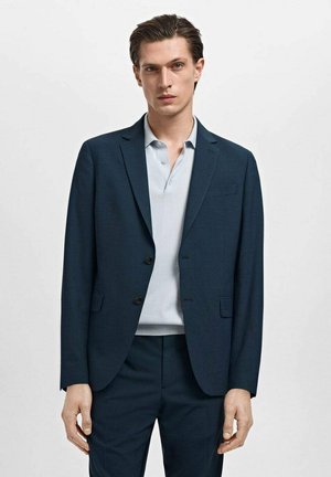Chaqueta de traje azul marino con dos botones, solapas en pico y un solo bolsillo, combinada con una camiseta polo azul claro. Textura de tela suave.