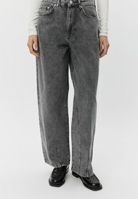 Sive visoke široke kavbojke z blede pranja, sprednjimi �žepi in gumbom za zapiranje. Imajo sproščen kroj in ravno silhueto.