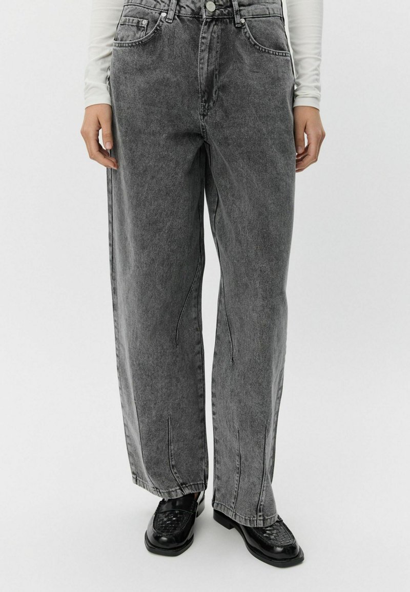 Sive visoke široke kavbojke z blede pranja, sprednjimi žepi in gumbom za zapiranje. Imajo sproščen kroj in ravno silhueto.