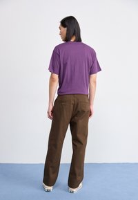Paarse korteblazert-shirt gecombineerd met bruine rechte broek. Het T-shirt heeft een ontspannen pasvorm; de broek heeft een achterzak en subtiele stiksels.