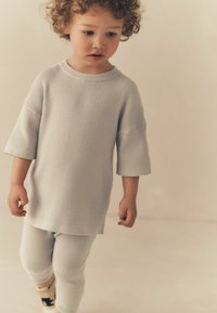 Jasnoszara, prążkowana koszulka z krótkim rękawem, w komplecie z pasującymi prążkowanymi legginsami. Ubranie ma luźny krój i miękką teksturę.