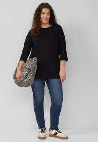 Zwarte long-sleeve top, blauwe jeans en beige sneakers met zwarte accenten. Houdt een tas met een luipaardprint en een slouchy ontwerp vast.