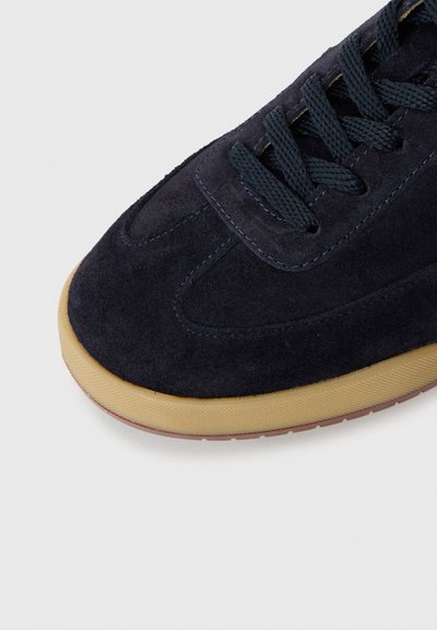 Mørkeblå semsket sneakers med teksturert gummisåle og matchende mørkeblå snører på hvit bakgrunn.