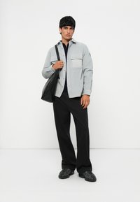 Gray button-up shirt with a front pocket, black t-shirt underneath, black wide-leg pants, and black bag. Footwear features textured detailing.