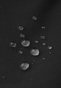 Tejido negro texturizado con varias gotas de agua claras en la superficie, mostrando la resistencia al agua y la durabilidad del material.