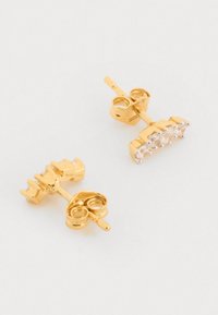 Náušnice v zlatej farbe so študom, ktoré obsahujú klaster piatich priehľadných rhinestones, s okrúhlymi zátkami pre bezpečné nosenie. Hladký kovový povrch.