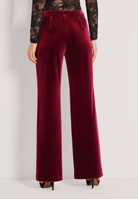 Bordeaux fluwelen wijde broek met een gestructureerd oppervlak en een elastische tailleband, voorzien van zijzakken en een relaxte pasvorm.