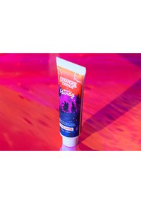 Tuba kremu do rąk z wzorem nawiązującym do "Stranger Things", z gradientem od pomarańczowego do fioletowego, sylwetkami postaci i białą nakrętką. 30 ml.