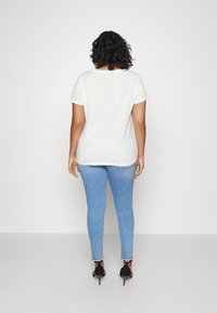 Camiseta blanca de algodón con mangas cortas, combinada con pantalones vaqueros ajustados de mezclilla azul claro y zapatos de tacón alto negros. Diseño sencillo y ajustado.