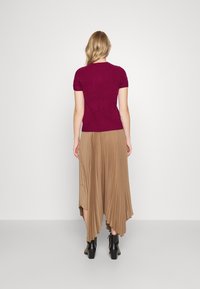 Kortärmad kabelstickad tröja i burgundy kombinerad med en flödande, plisserad beige kjol med asymmetrisk fåll. Svarta ankelboots kompletterar looken.