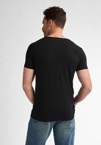 Tricou negru cu mânecă scurtă și guler larg, realizat dintr-un material neted. Purtați cu blugi de denim albaștri deschiși, având buzunare pe spate.