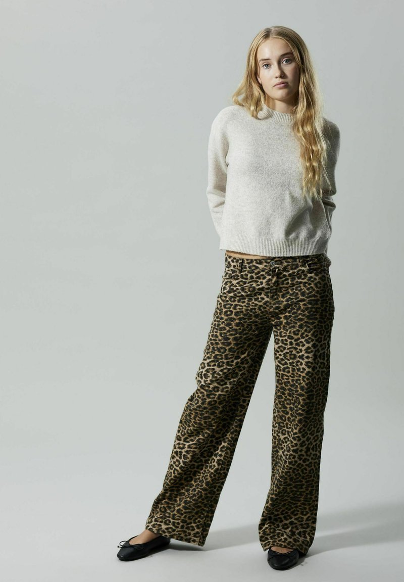 Suéter de lana beige con cuello redondo, combinado con pantalones de pata de elefante de estampado de leopardo con patrones en negro y marrón. Zapatos planos negros.