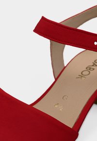 Κόκκινο σουέντ σανδάλι με λουράκι στον αστράγαλο. Διαθέτει απαλή υφή, ανοιχτό σχέδιο και χρυσό λογότυπο στην εσωτερική σόλα.