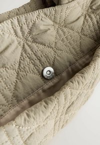 Intérieur d'un sac matelassé beige clair mettant en valeur un bouton-pression en métal central et des détails cousus le long des bords.
