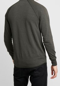 Koszula z długim rękawem w ciemnooliwkowym kolorze, wykonana z miękkiego materiału o lekko fakturowanej powierzchni, z rękawami raglanowymi i zaokrąglonym dołem.