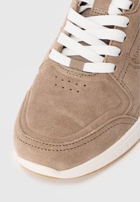 Brązowe zamszowe trampki z białymi sznurowadłami, perforowaną cholewką oraz przeszyciami. Posiadają białą gumową podeszwę i teksturowany wierzch.