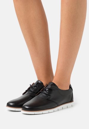 Zapatos de cuero negro con cordones, punta redondeada, suela de goma blanca y diseño minimalista. Textura suave con detalles de costura sutiles.