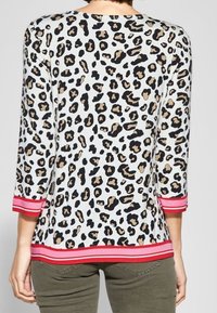 Top med leopardmönster och trekvartsärmar, vit botten med svarta och bruna fläckar och rödrandig nederkant. Slät tyg och avslappnad passform.