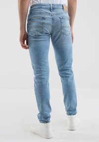 Vaqueros de mezclilla azul claro con corte ajustado, que cuentan con bolsillos traseros y detalles de costura, combinados con calzado blanco.
