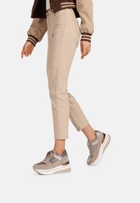 Pantaloni cropped beige abbinati a sneaker grigie e metalliche. Le sneaker presentano una superficie liscia, un design con lacci e una suola bianca chunky.