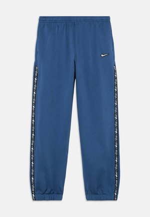 Pantaloni sport albastri Nike cu talie și manșete elastice, dungi laterale negre cu text repetat „Nike” alb și un mic logo Nike Swoosh alb.