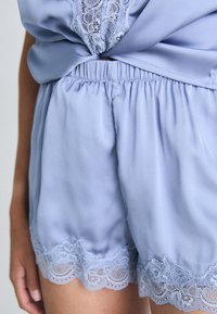 Ljusblå shorts i mjukt tyg, med elastisk midja och en delikat spetsdetalj i nederkant för en texturerad effekt.