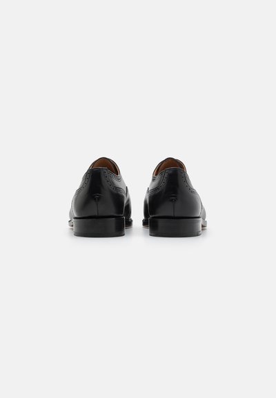 Scarpe brogue in pelle nera con perforazioni decorative, punte arrotondate e tacchi impilati. Texture liscia e finitura lucida.