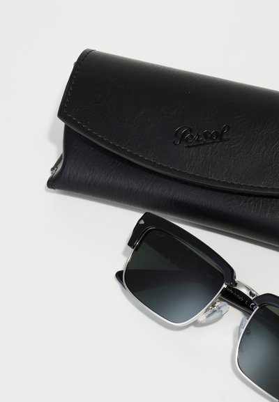 Ochelari de soare Persol negri cu lentile verzi, cadru unghiular negru, accente argintii și o carcasă din piele neagră cu logo embossat.