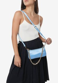Lys blå læder crossbody taske med en blank overflade, justerbar strop og sølv kædeldetaljer. Rektangulær form med lynlåslukning.
