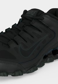 Črni Nike športni čevelj z teksturiranim zgornjim delom, z vezalkami in Velcro trakom, s vidnim zračno blažilno podplatom in diskretno oznako Swoosh.