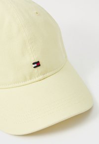 Casquette de baseball jaune en tissu texturé, avec un petit logo brodé comprenant des rayures rouges, blanches et noires sur le devant.