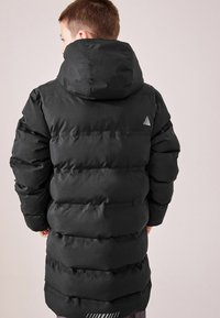 Doudoune noire avec capuche, design matelassé horizontal, texture lisse et petit logo blanc sur le haut du dos.