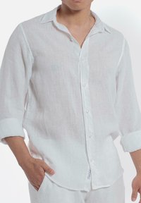 Witte linnen blouse met lange mouwen, knoopsluiting aan de voorkant en een zachte, gestructureerde afwerking. Heeft opgerolde manchetten en een ontspannen pasvorm.