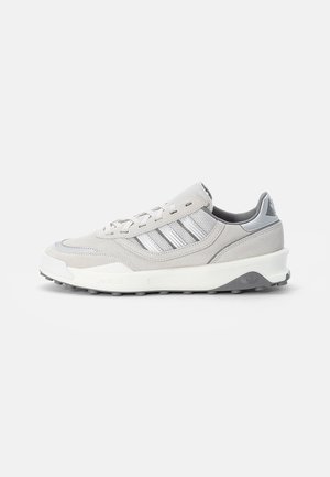 Jasnoszare i białe sneakersy Adidas z panelami z zamszu i siateczki, zawiązywane na sznurówki, z amortyzowaną podeszwą na białym tle.