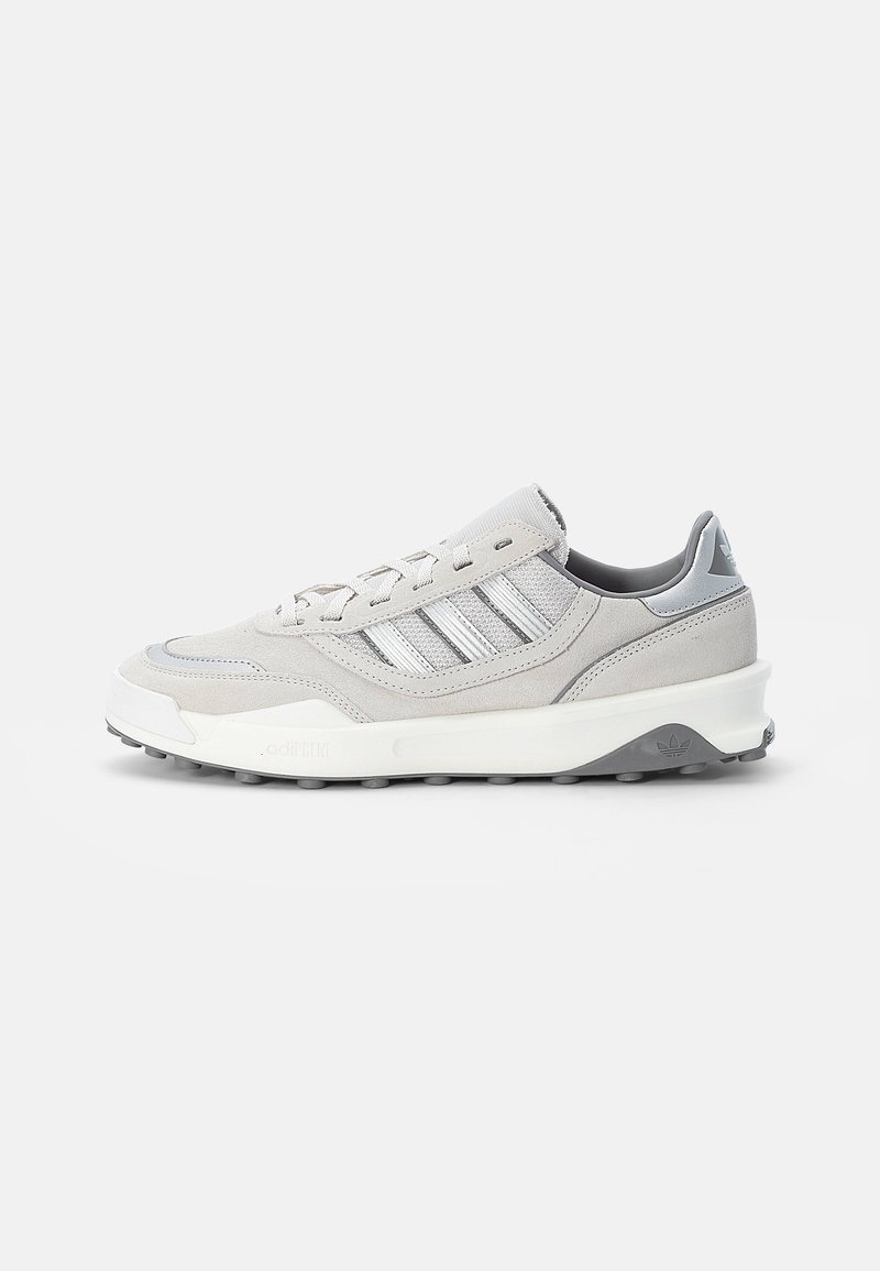Hellgrauer und weißer Adidas Sneaker mit Velours- und Mesh-Einsätzen, Schnürverschluss und gepolsterter Sohle vor weißem Hintergrund.