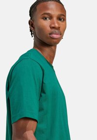 Zelené bavlněné tričko s krátkými rukávy, kulatým výstřihem a volným střihem. Hladká textura a rovnoměrná barva s minimálními detaily.