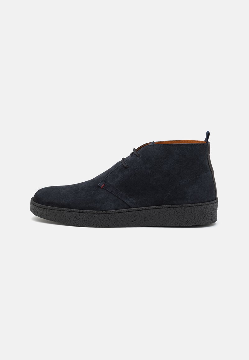 Botines de ante azul oscuro con una suela de goma negra texturizada, un diseño sencillo de cordones y un interior marrón en contraste.