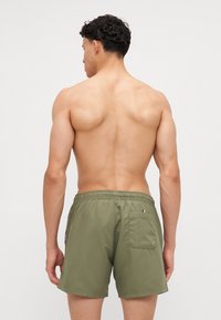 Shorts de bain pour hommes en vert olive, fabriqués en tissu léger. Dotés d'une taille élastique, d'une poche au dos et d'un design épuré.