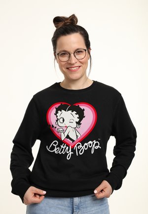 Felpa nera con una grafica di Betty Boop all'interno di un cuore rosa, con testo "Betty Boop" sotto, realizzata in cotone o materiale simile.