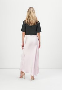 Uma t-shirt cinza escura combinada com uma saia maxi de seda rosa pálido. A saia tem um design fluido e um brilho subtil, complementada por saltos nude.